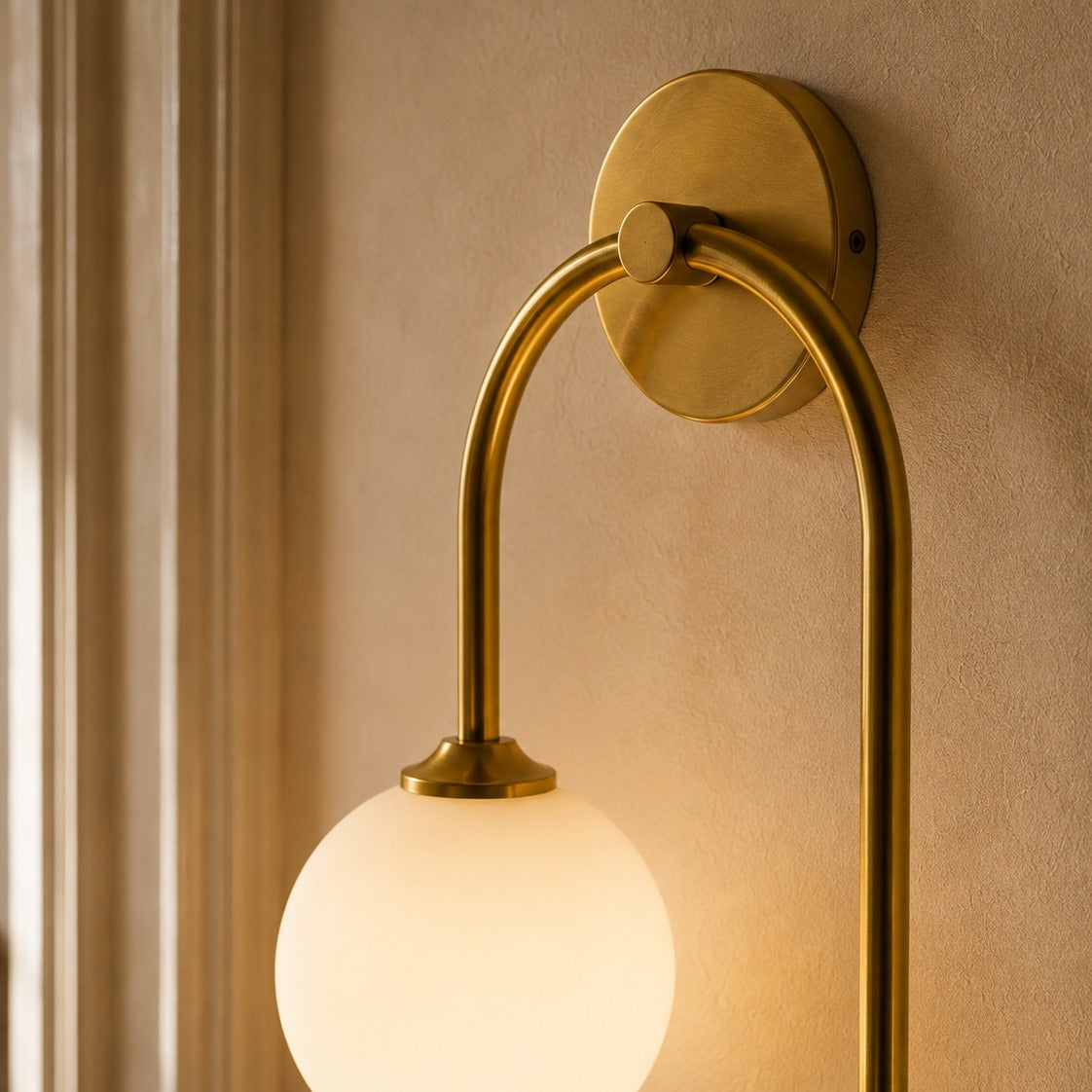 Close-up of a gold glass ball wall light globe glowing against a plaster wall