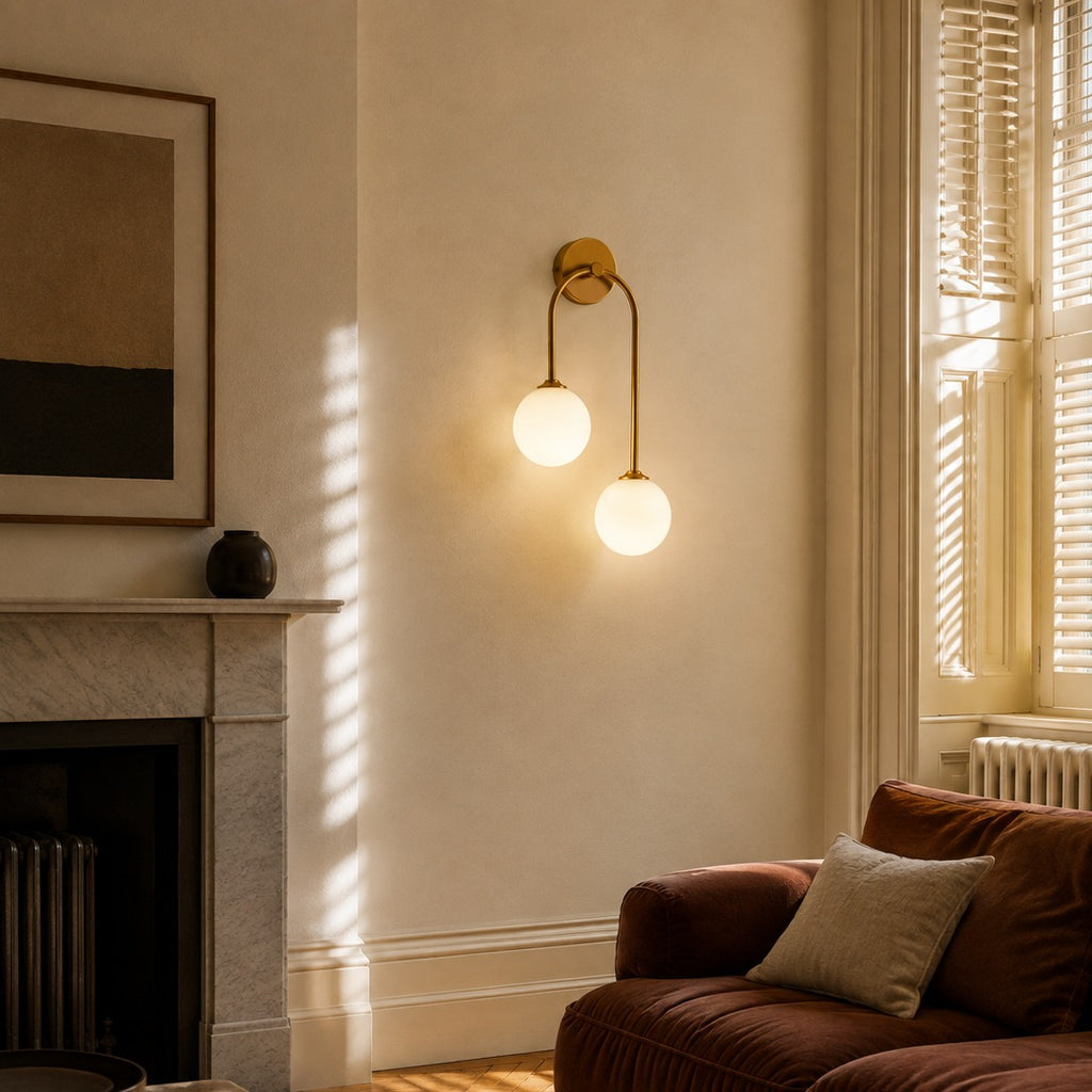 Gold glass ball double wall light glowing beside a fireplace and brown velvet armchair