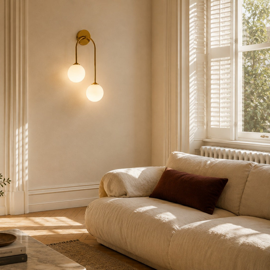 Gold glass ball double wall light above a low sofa in a sunlit period living room