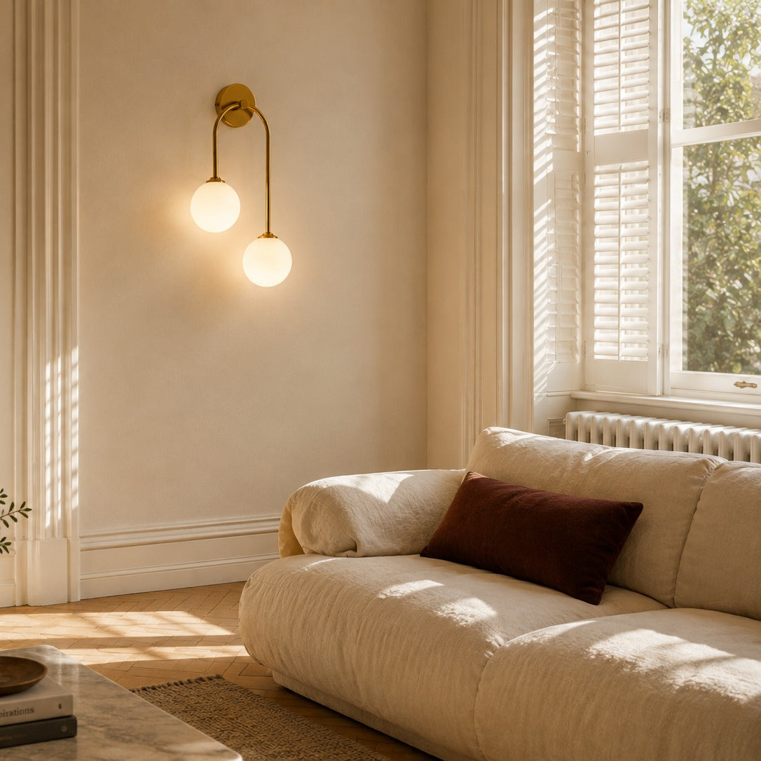 Gold glass ball double wall light above a low sofa in a sunlit period living room